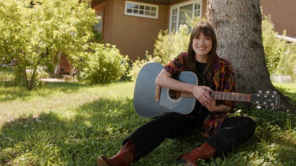 Hearse Chasing film image; woman leaning against a tree trunk playing a guitar