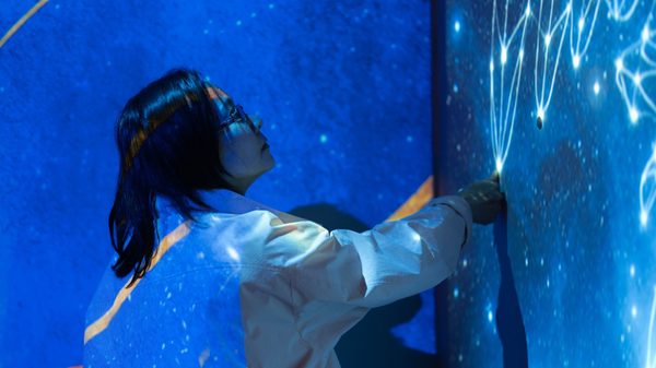 person pressing their thumb against a wall with the night sky projected on it