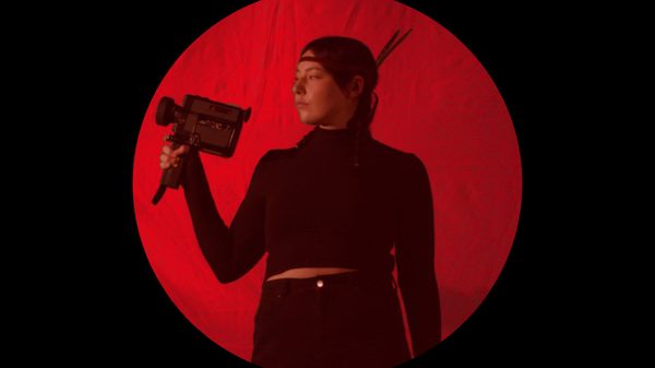 The First Female Indigenous Pornographer film image; woman holding a video camera backlit by a red spotlight