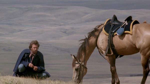 Dances with Wolves film image; man sitting by a horse eating grass