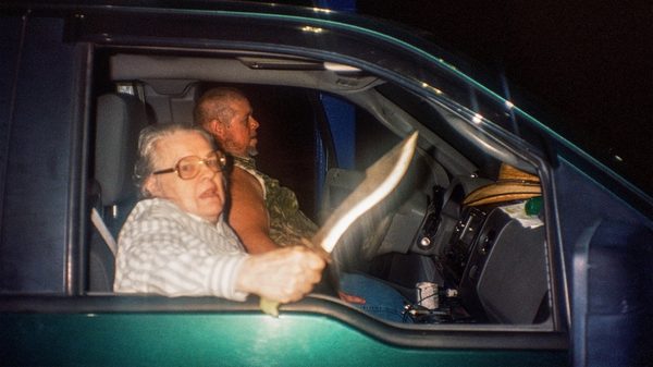 The Python Hunt film image; person in the passenger seat of a car holding a large knife