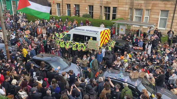 Everybody to Kenmure Street film image; a large crowd surrounding vehicles in the street