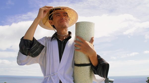Aruku - I Walk film image; man holding a rolled-up yoga block