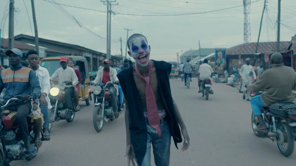Crocodile film image; person in clown makeup staggering down a street