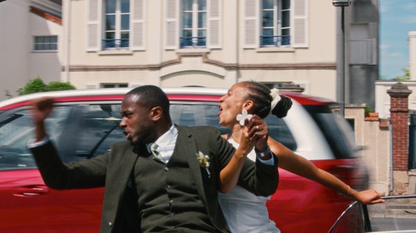 Dao film image; bride and groom hiding behind a car