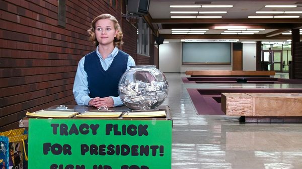 Election film image; teenaged girl standing behind a small desk in a school hallway