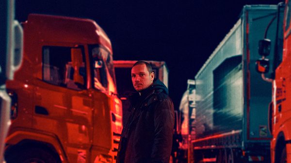 Flesh and Fuel film image; man standing next to parked semi trucks