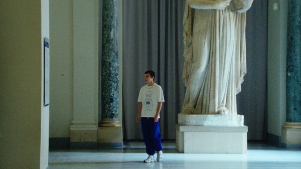 La Gradiva film image; man standing next to a large marble statue