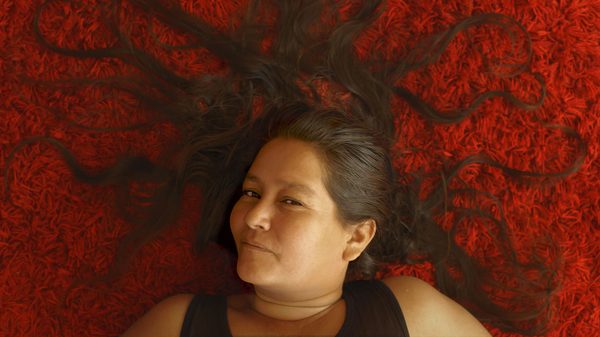 A Place of Absence film image; woman laying down on red carpet with her hair sprawled out