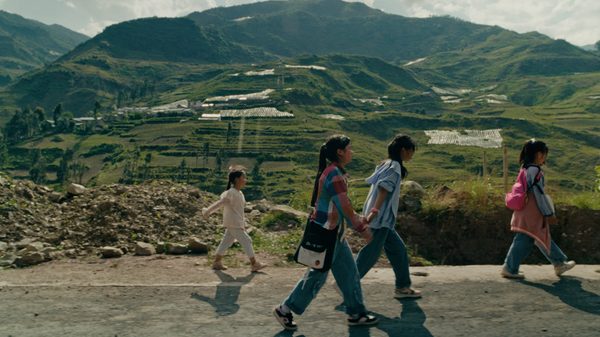 Whispers in May film image; children walking on pavement with a mountain in the distance