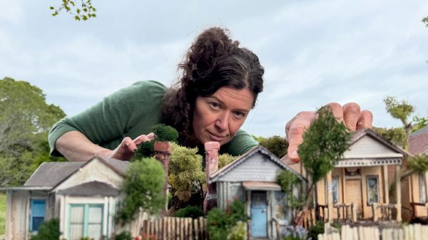 Yo film image; woman leaning over a small model neighbourhood