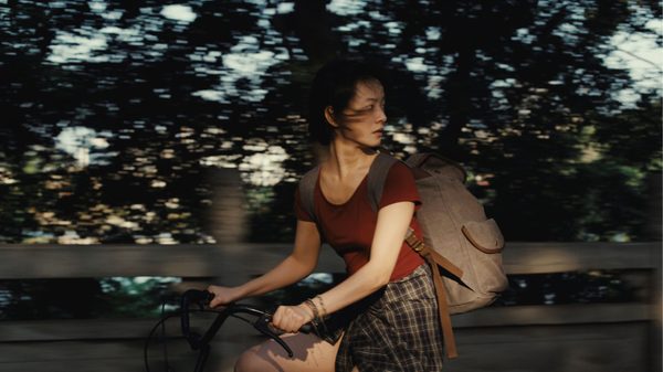 A Girl Unknown film image; woman riding a bicycle looking over her shoulder