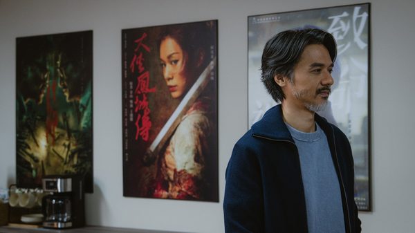 Afterpiece film image; man standing by a wall with posters on it