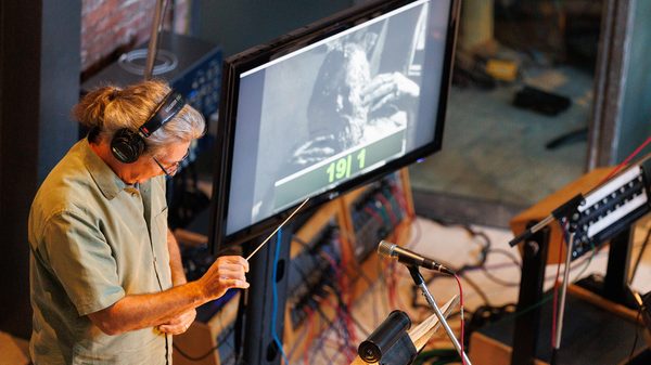 a person with a conductor's wand standing next to a large monitor