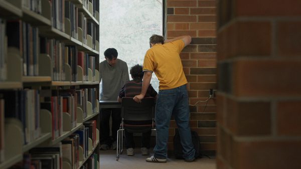Clubfoot film image; three people at the end of an aisle in a library