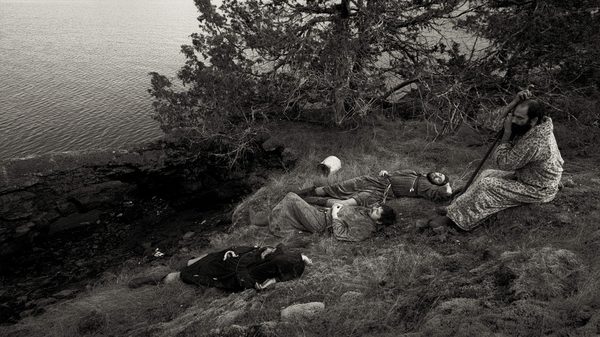 Gasmask film image; people lying down on grass by water
