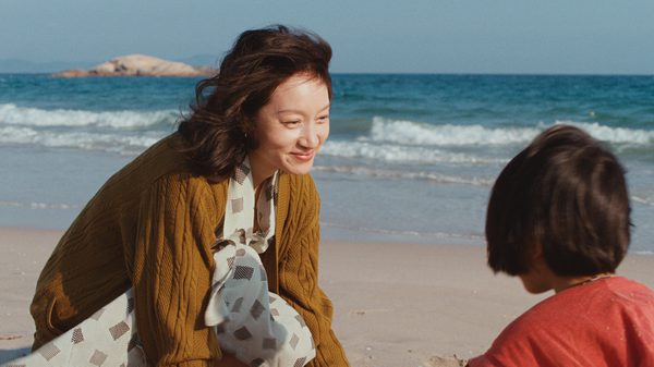 A Girl Unknown film image; woman crouching by a child on the beach