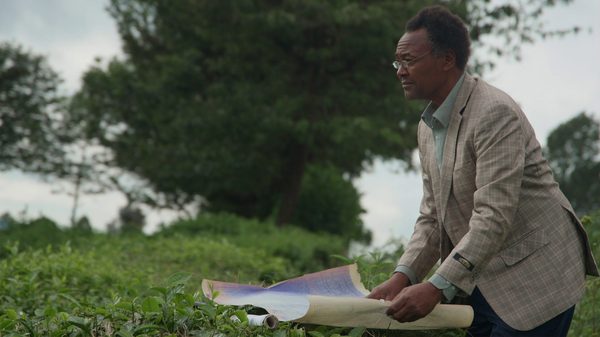 Kikuyu Land film image; man spreading out a sheet of paper on grass