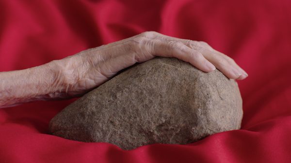 Kontrewers film image; hand resting on a rock nestled in red fabric