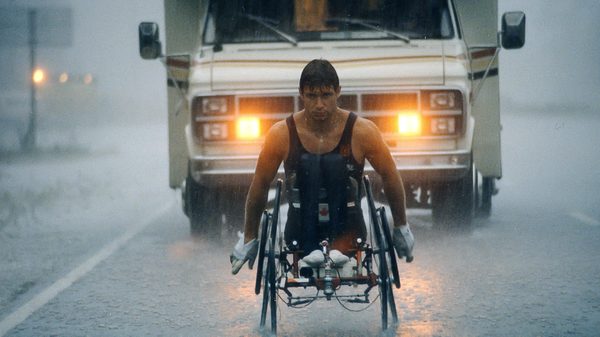 Man in Motion film image; man using wheelchair down a street in the rain