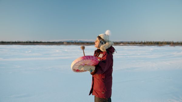 Nitassinan film image; person standing in the snow banging on a hand drum