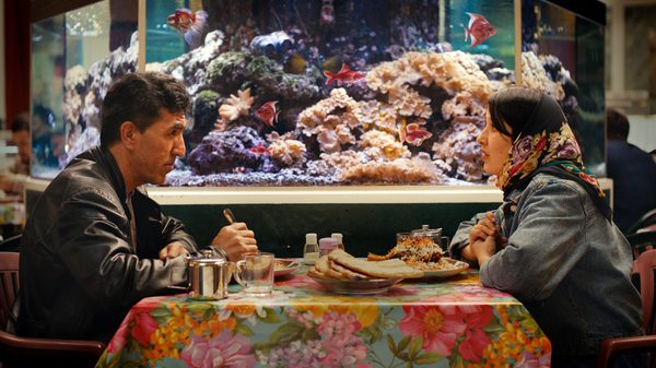 No Good Men film image; two people sitting at a dinner table next to an aquarium
