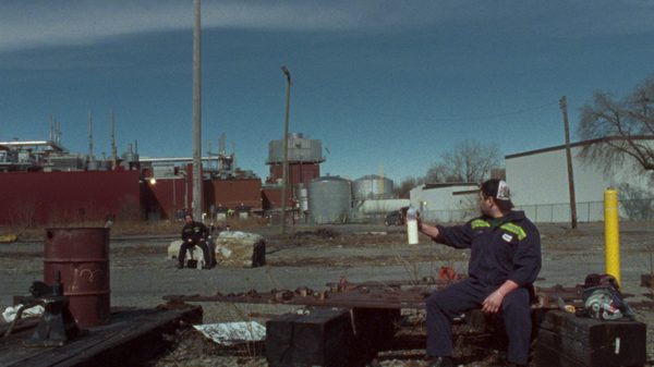 Pique-Nique film image; man sitting across a street from another person