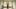 Rebecca Horn film image; woman in a empty room holding out her arms with makeshift scissorhands