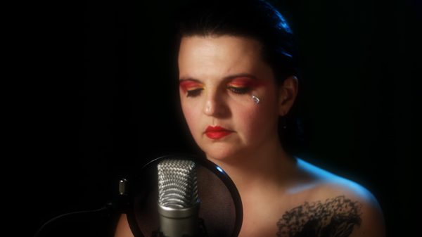 Self-Preserving Nudity film image; woman in front of a microphone