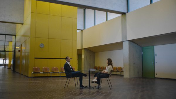 Sometimes, I Imagine Them All at a Party film image; two people sitting at a small table