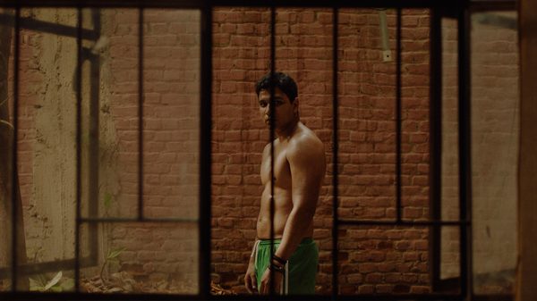 That Shadow Fading film image; shirtless man behind the bars of a fence