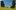 Wild Horse Nine film image; two people sitting in long grass by two large stone head statues