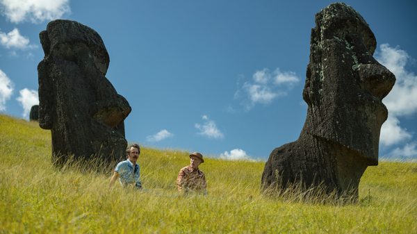 Wild Horse Nine film image; two people sitting in long grass by two large stone head statues