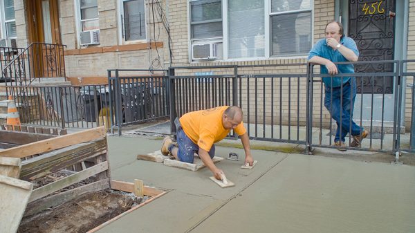 The History of Concrete film image; man smoothing just-poured concrete sidewalk