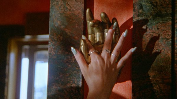 Twin Snakes film image; person's hand reaching up for a metallic hand on a post