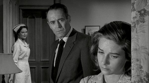 The Wrong Man film image; woman leaning sadly against a wall while two people watch her