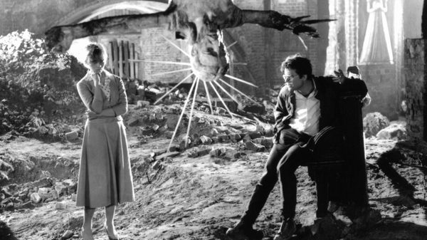 Ashes and Diamonds film image; man and woman in a field with a statue hanging upside down between them