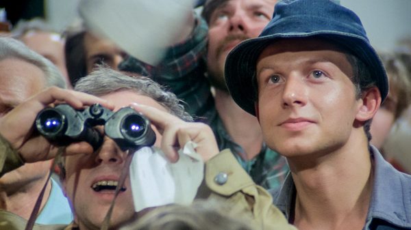 Man of Iron film image; man leaning into another man who's looking through binoculars
