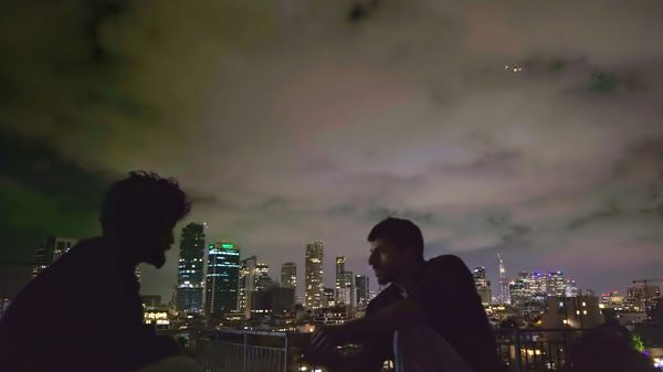 Naza film image; two people sitting in a foggy night with skyscrapers in the background