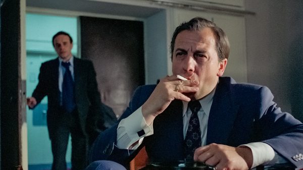 Rough Treatment film image; man walking through a door to another man smoking a cigarette