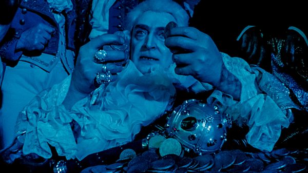 The Wedding film image; person wearing a large ruffled collar under blue lighting